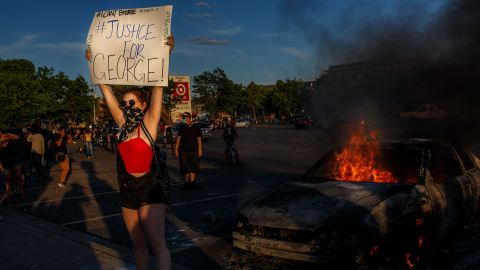 A protester hold sign board "Justice for George" into a fire outside a Target store near the Third Police Precinct on May 28, 2020 in Minneapolis, Minnesota, during a demonstration over the death of George Floyd.