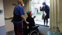 MISSION HILLS, CALIFORNIA - DECEMBER 24: Juliet Babayan holds a gift for her sister Violet Bonyad as they visit through a window at the Ararat Nursing Facility on Christmas Eve on December 24, 2020 in Mission Hills, California. Due to the COVID-19 pandemic, family members are not allowed to visit relatives inside the facility but are able to hold personal visits at the window. (Photo by Mario Tama/Getty Images)