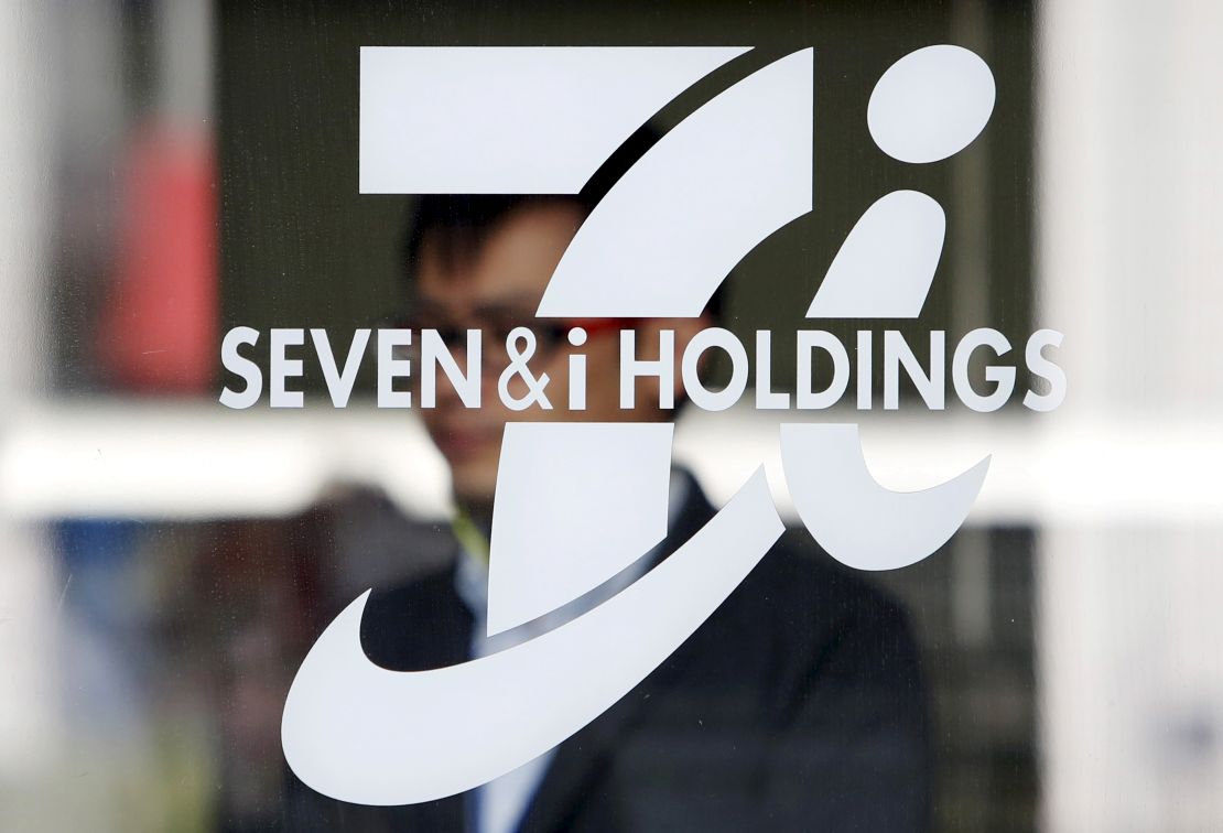A shopper is seen behind a Seven & I Holdings' logo at a 7-Eleven convenience store in Tokyo, Japan, April 6, 2016.