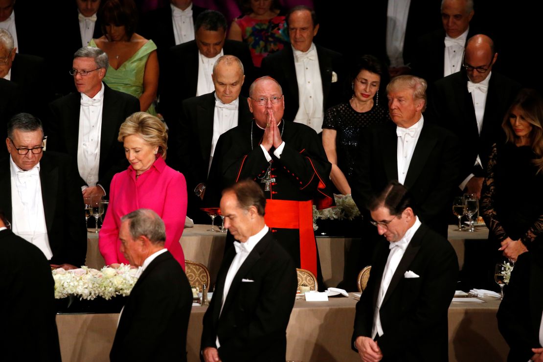 Kardinal New York Timothy Dolan, tengah, menggenggam tangannya dalam doa saat ia mengambil tempat di antara Hillary Clinton dan Donald Trump di acara makan malam Alfred E. Smith Memorial Foundation di New York City pada tanggal 20 Oktober 2016.