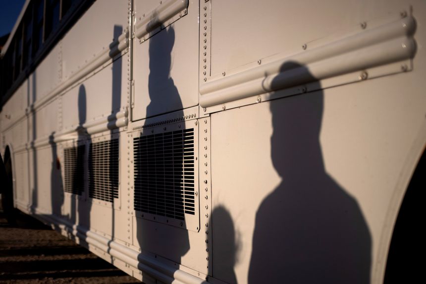 The shadows of asylum-seeking unaccompanied minors are seen amid shadows of adult migrants from Central America as they await transport after crossing the Rio Grande river into Penitas, Texas, on March 12, 2021.