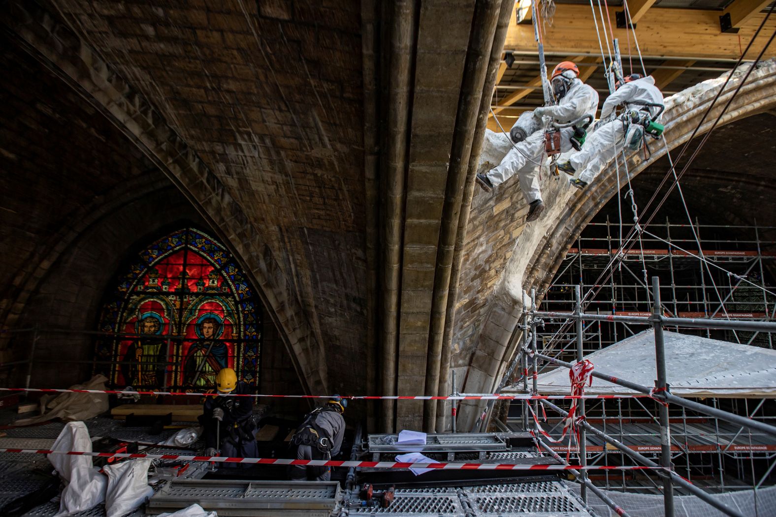 Workers plaster stonework as they rappel down a vault inside Notre Dame in April 2021.