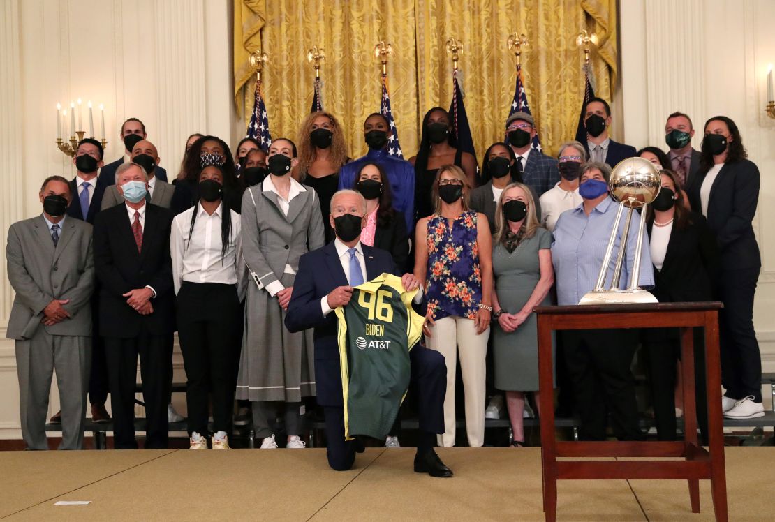 US President Joe Biden holds up a jersey he was gifted as he kneels for a group photograph with members of the Seattle Storm 2020 WNBA Championship women’s basketball team at the White House in Washington, U.S., August 23, 2021.