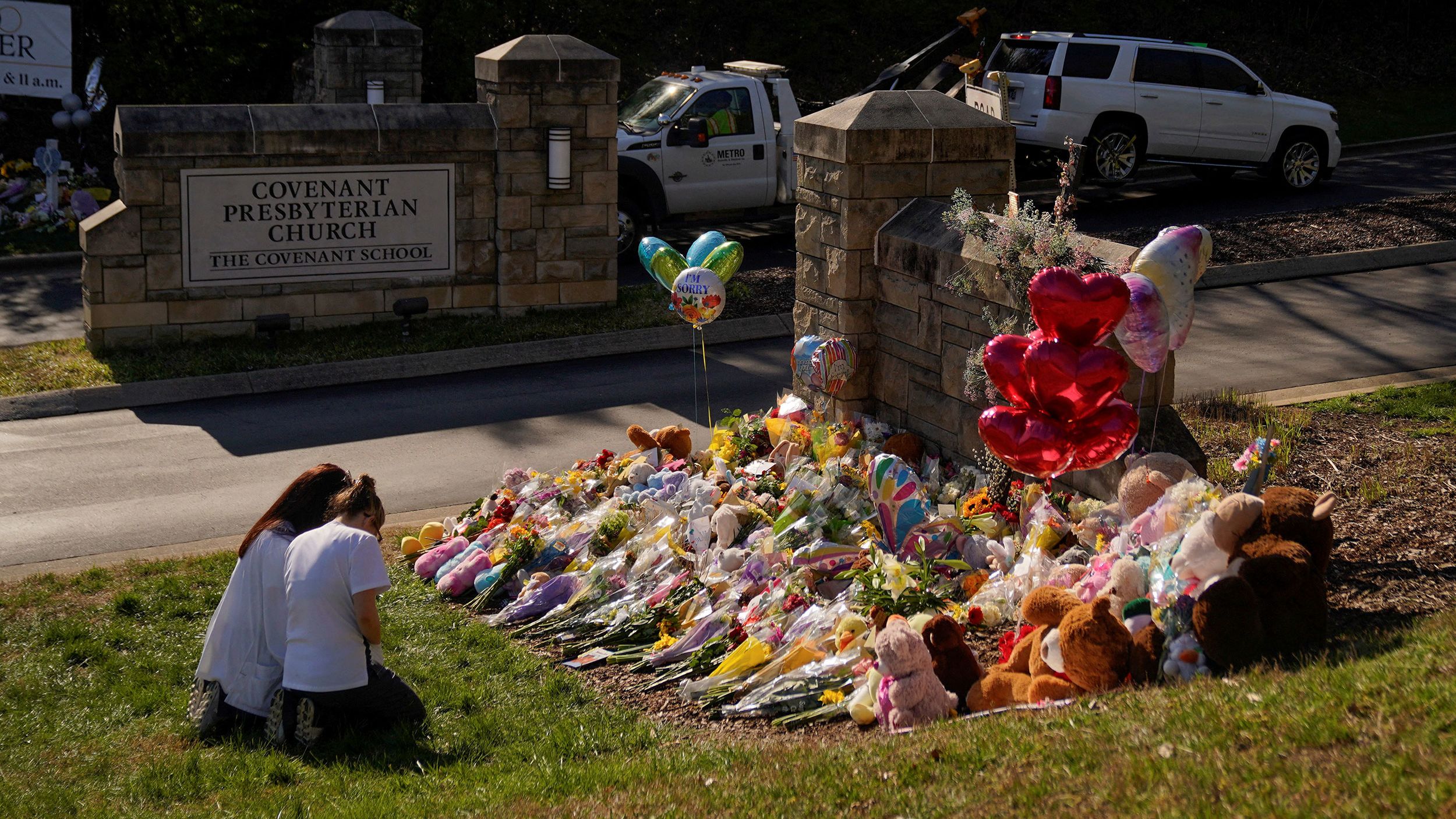 A vehicle is towed from the property as community members pray while visiting a memorial at the school entrance after a deadly shooting at the Covenant School in Nashville.