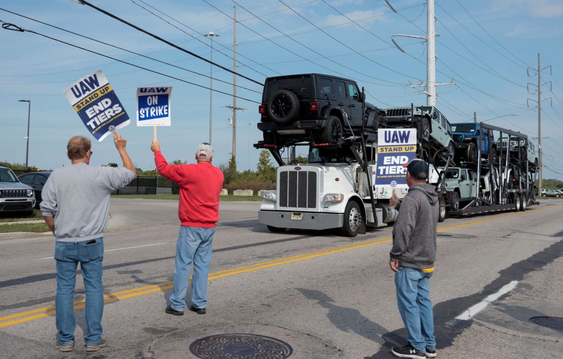 A car hauler transporting Jeep Wranglers drives past striking United Auto Workers members outside the Stellantis Jeep Plant in Toledo, Ohio, during the 2023 strike. One of the two factories at that assembly complex is about to lose one of the two shifts that builds the Jeep Gladiator.