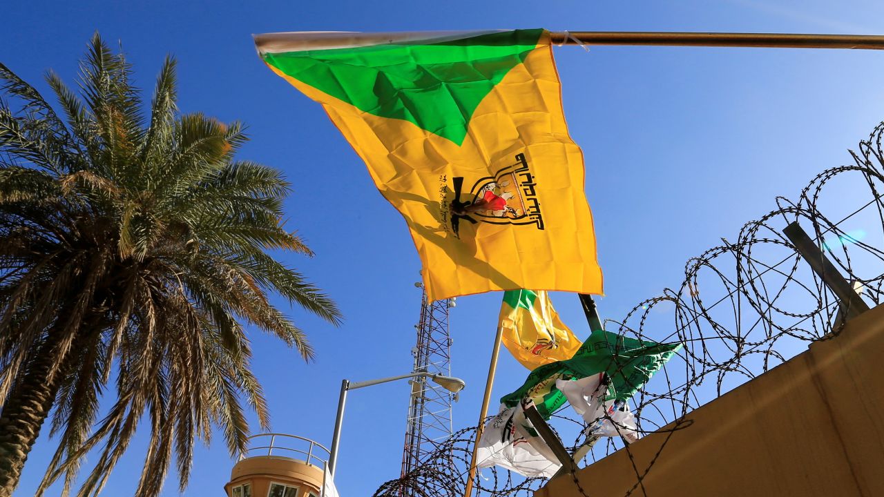 FILE PHOTO: A member of Hashd al-Shaabi (paramilitary forces) holds a flag of Kataib Hezbollah militia group during a protest to condemn air strikes on their bases, outside the main gate of the U.S. Embassy in Baghdad, Iraq December 31, 2019. REUTERS/Thaier al-Sudani/File Photo