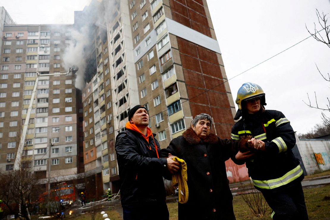 Firefighters in Kyiv help a woman to leave a building damaged by Russian strikes.