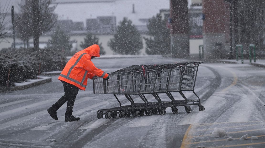 A supermarket employee returns shopping carts in the Market Basket parking lot in Plymouth, Massachusetts, during a fast-moving winter storm that hit the US Northeast February 13, 2024.