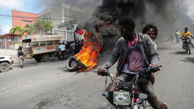 People drive past a burning blockade as demonstrators hold a protest calling for the resignation of Haitian Prime Minister Ariel Henry outside the Canadian Embassy, in Port-au-Prince, Haiti February 25 2024. REUTERS/Ralph Tedy Erol