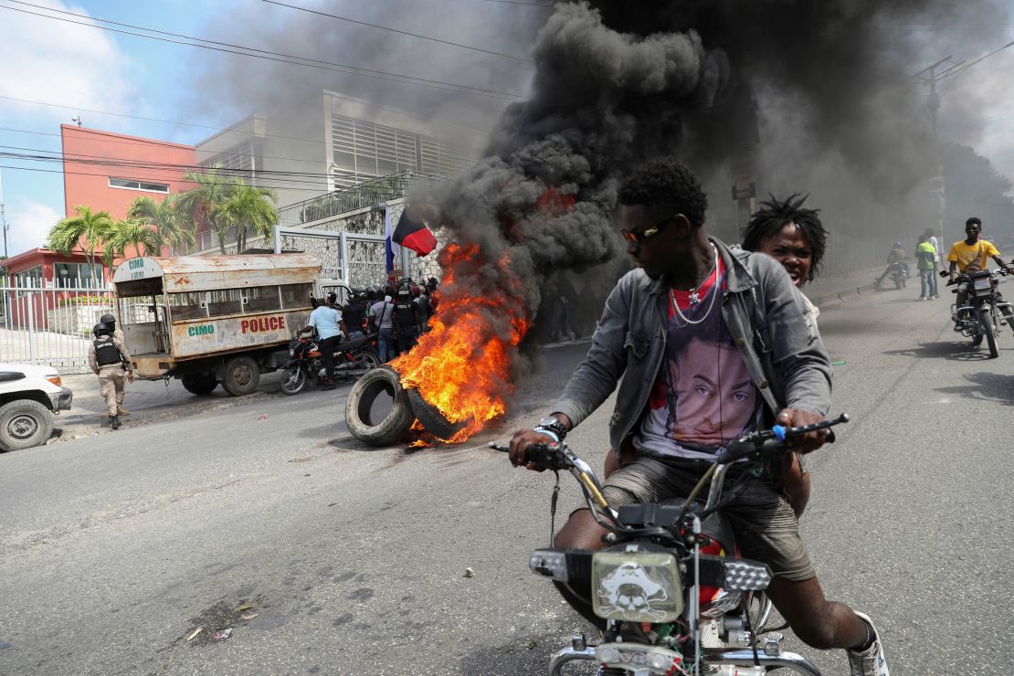 People drive past a burning blockade as demonstrators hold a protest calling for the resignation of Haitian Prime Minister Ariel Henry outside the Canadian Embassy, in Port-au-Prince, Haiti February 25 2024.