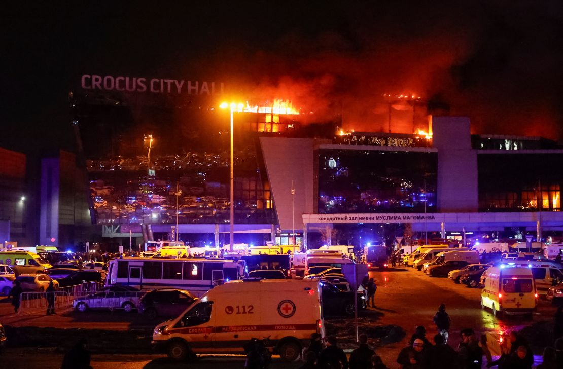 Ambulances and vehicles of Russian emergency services parked at the burning Crocus City Hall concert venue.