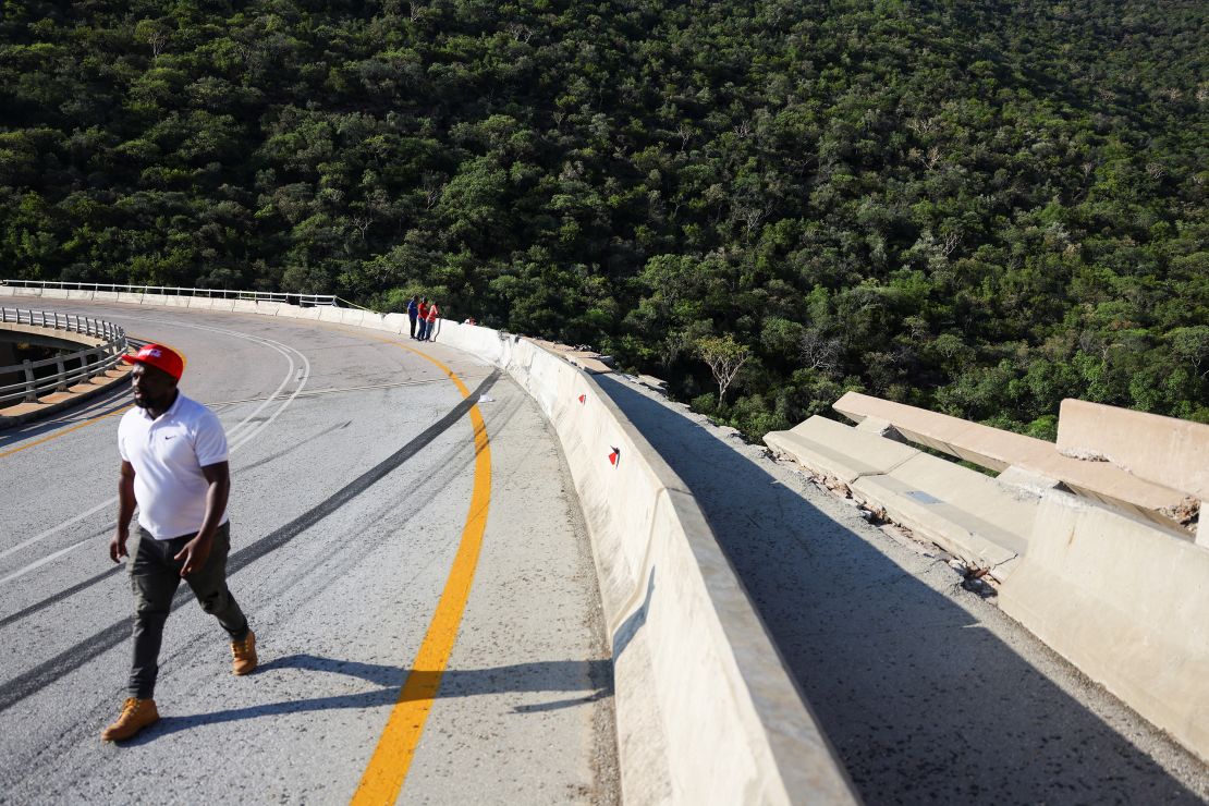 A man walks past the damaged part of the bridge, where the bus crashed through barriers. eiqrtidiqekinv