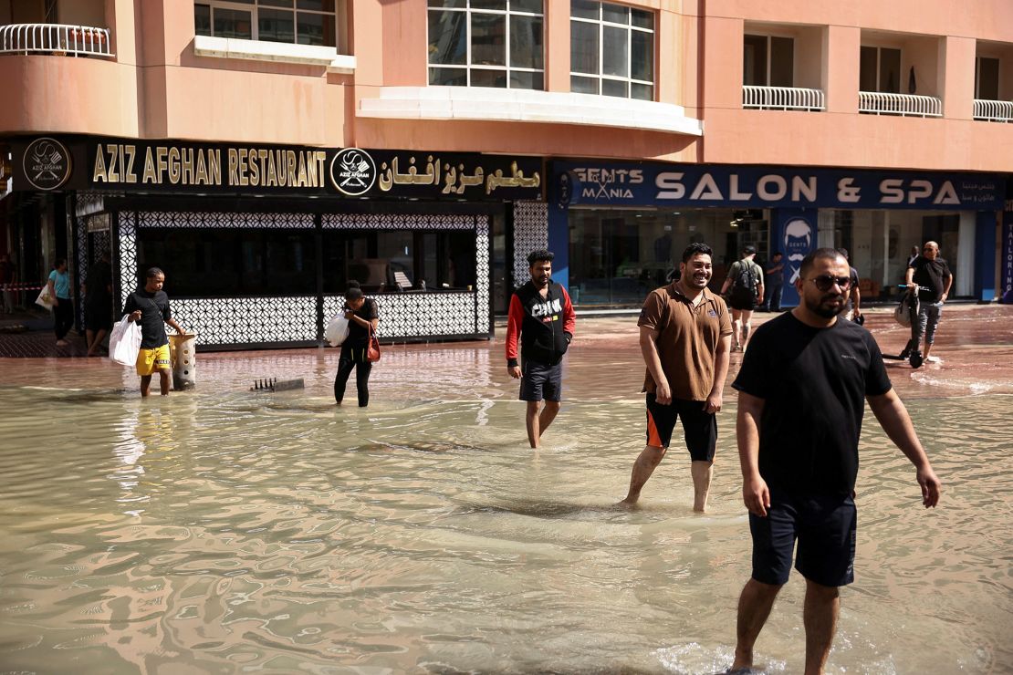 People walk through lingering floodwaters caused by heavy rains, in Dubai on April 17, 2024.