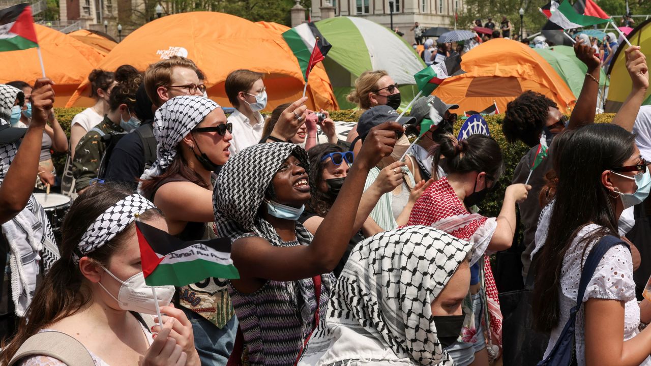 A group of students stands in a dense crowd. Behind them, tents are visible. 