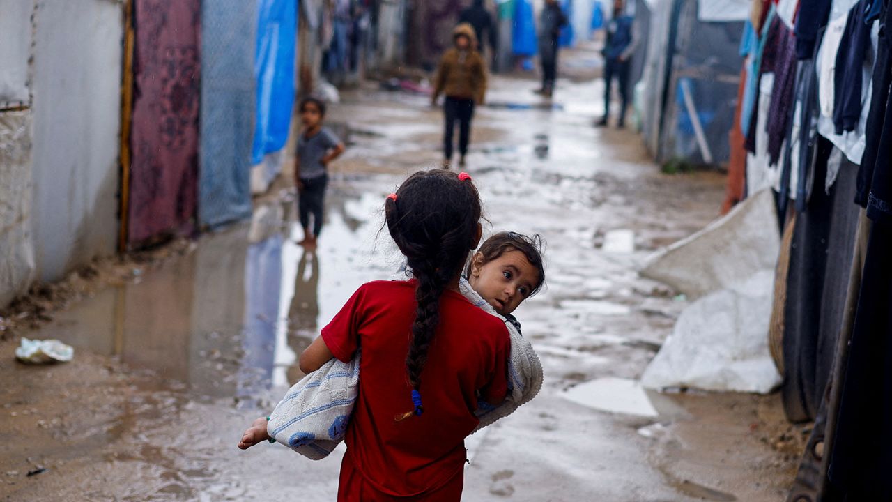 A displaced Palestinian girl holds a child as she walks at a tent camp on a rainy day, amid the ongoing conflict between Israel and Hamas, in Rafah, in the southern Gaza Strip, on May 6.