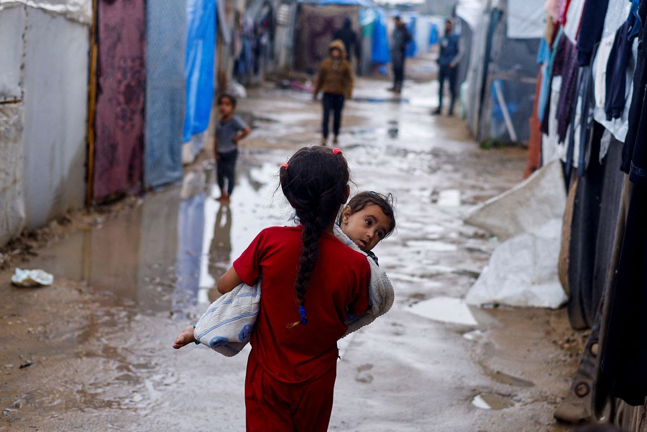 A displaced Palestinian girl holds a child as she walks at a tent camp on a rainy day, amid the ongoing conflict between Israel and Hamas, in Rafah, in the southern Gaza Strip, on May 6.