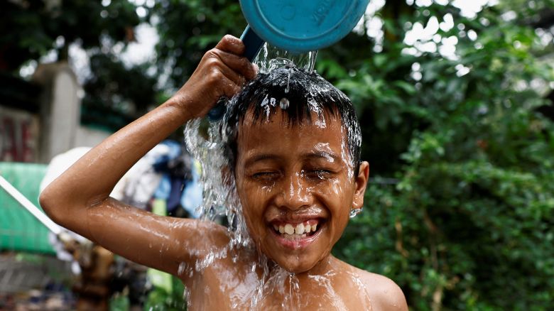 A boy reacts as he pours water on himself at a public well to cool down, amid the hot weather, at a densely populated area in Jakarta, Indonesia, May 16, 2024. REUTERS/Willy Kurniawan