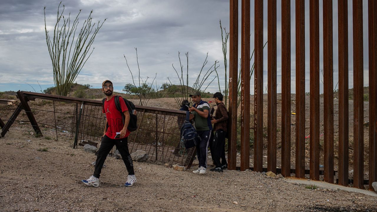 A smuggler stands in the background as asylum-seeking migrants from India cross the Border Wall into the United States from Mexico, in Ruby, Arizona, U.S., June 26, 2024. REUTERS/Adrees Latif