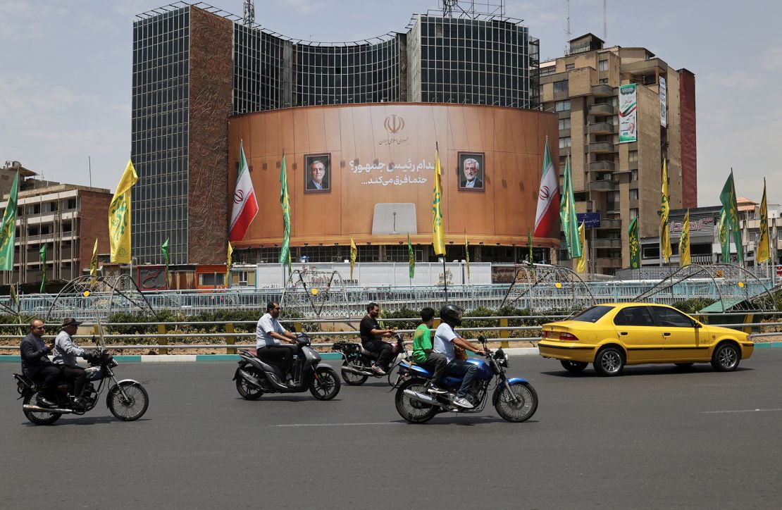 On a street in Tehran, Iran, on Monday, people drove past a billboard featuring photos of presidential candidates Masoud Pezeshkian and Saeed Jalili.