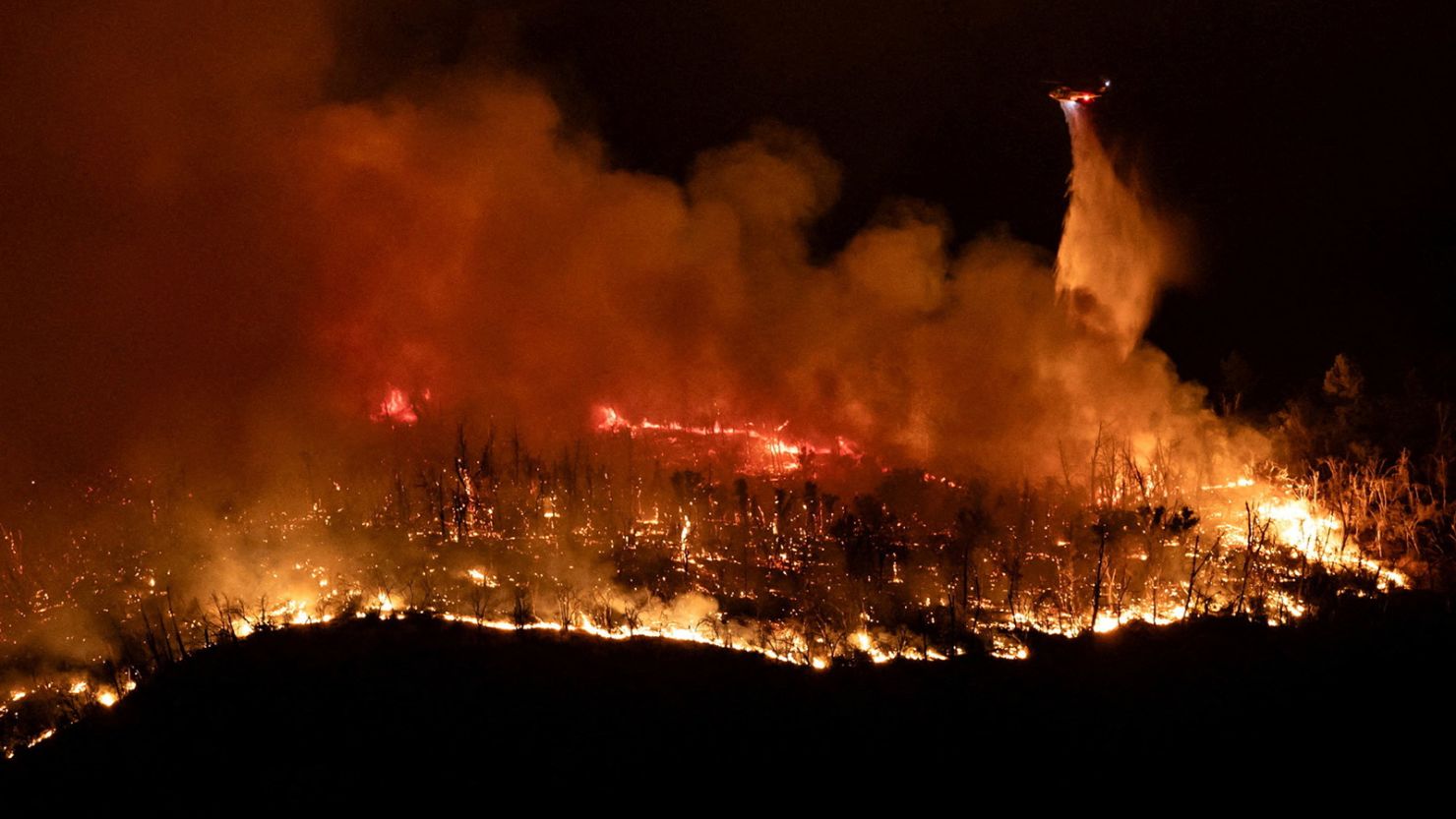 A helicopter drops water over the Thompson Fire as firefighters continue battling fire into the night near Oroville, California, on July 2.