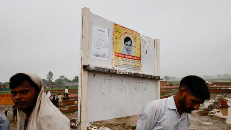 People stand near a poster of preacher Surajpal, also known as 'Bhole Baba' stuck on a board, at the site where believers had gathered for a Hindu religious congregation following which a stampede occurred, in Hathras district of the northern state of Uttar Pradesh, India, July 3, 2024. REUTERS/Anushree Fadnavis