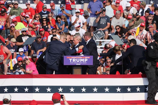 Trump is assisted by security personnel after the bangs were heard.