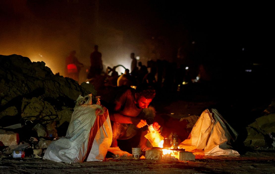 A man squats next to a fire, as Palestinians flee the eastern part of Khan Younis, after orders by Israeli army to evacuate their neighborhoods, in Khan Younis, in the southern Gaza Strip, on July 22, 2024.