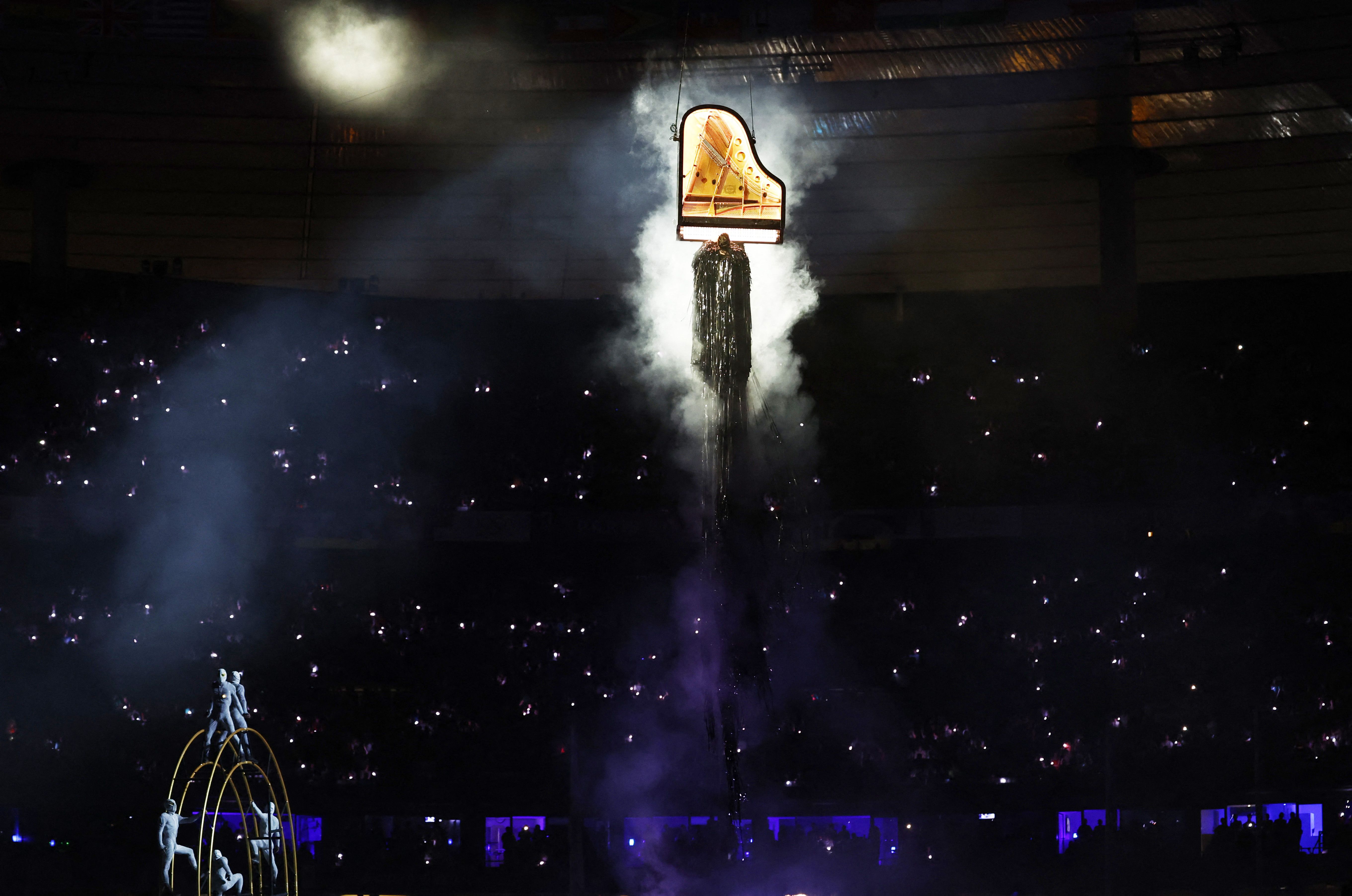 Alain Roche plays the piano while suspended from wires hanging from the stadium's roof.