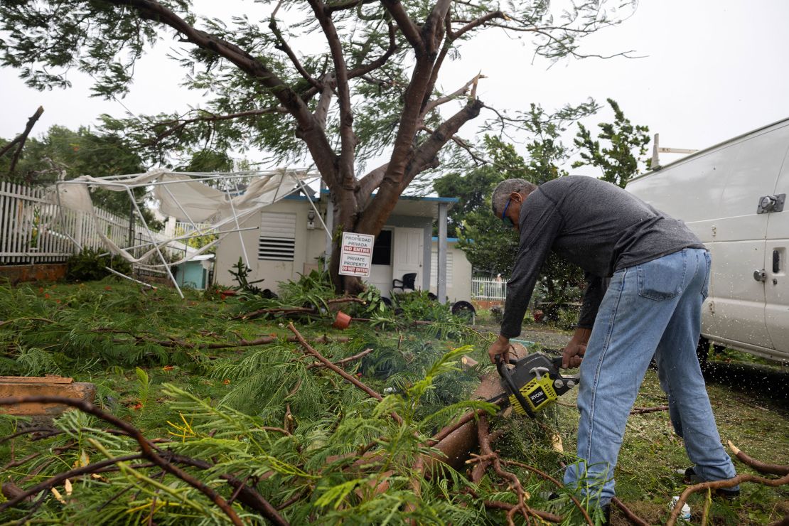 A man uses a chainsaw to clear branches from a tree in front of a house in the aftermath of Tropical Storm Ernesto in Fajardo, Puerto Rico, Wednesday.