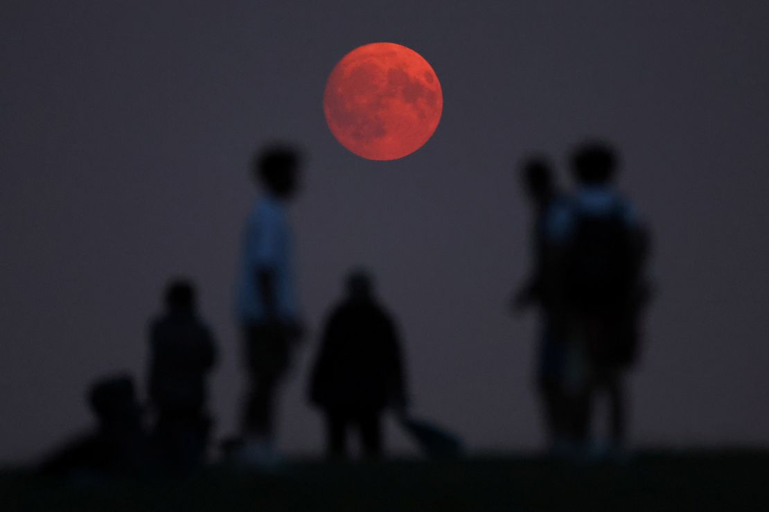 People view the moon as it rises, with a red glow attributable to smoke particles in the upper atmosphere from North American wildfires, a day ahead of the super blue moon, at Parliament Hill in London, August 18.