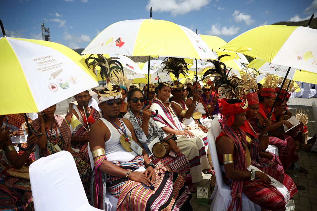 Crowds wait for the pope under yellow and white umbrellas.