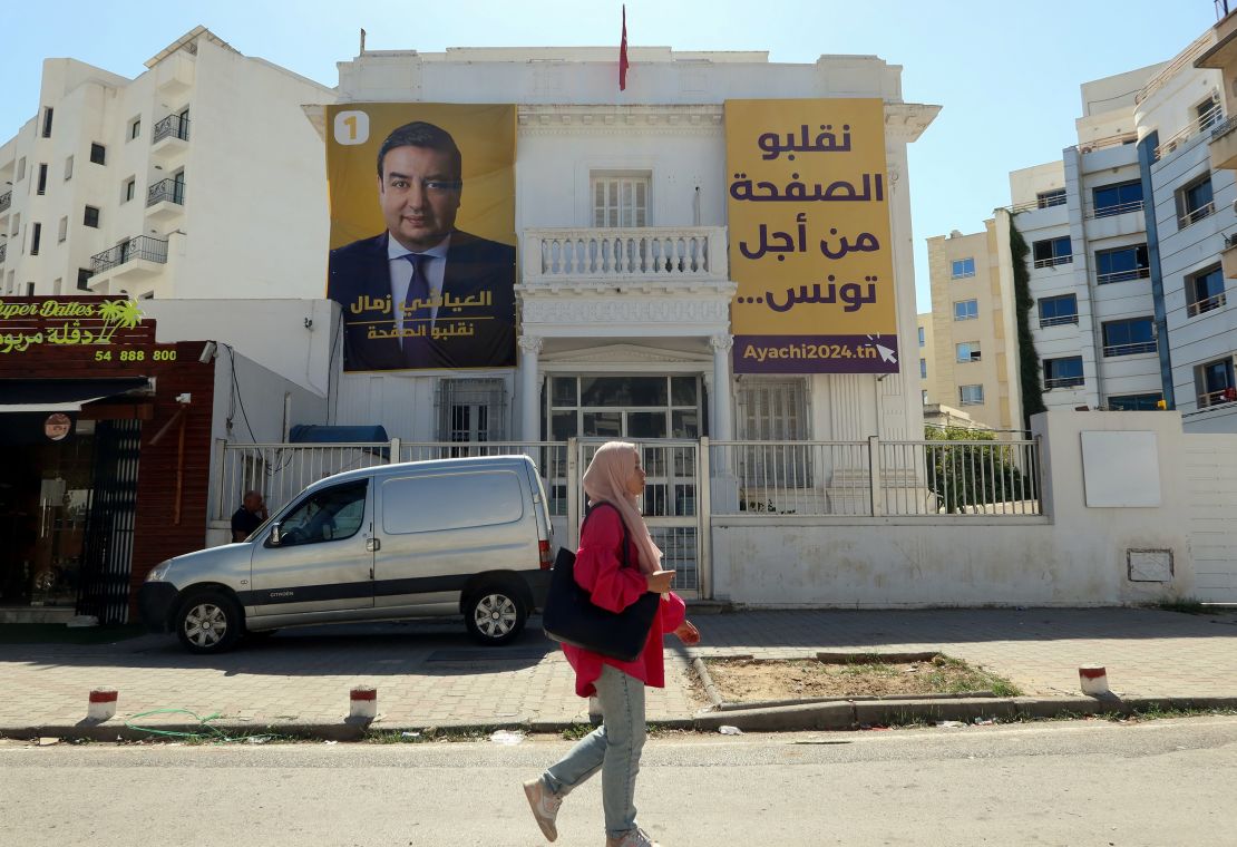 A woman walks past a poster depicting presidential candidate Ayachi Zammel, hanging on his party's Azimoun headquarters in Tunis on October 1, 2024.