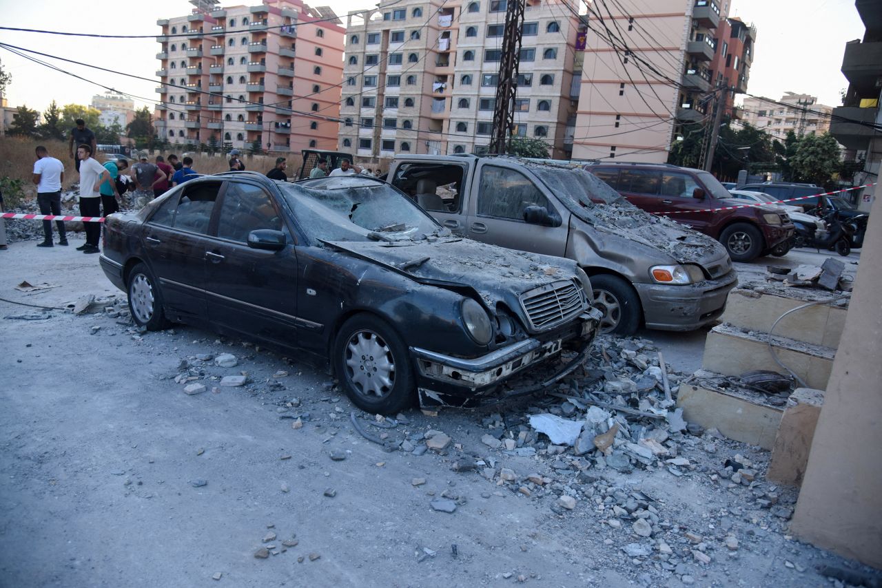 People stand near damaged vehicles at the site hit by an Israeli strike that, according to a security source, killed Saeed Atallah, a leader in Hamas' armed wing al-Qassam brigades, with three family members, in the northern city of Tripoli, Lebanon October 5, 2024. REUTERS/Omar Ibrahim