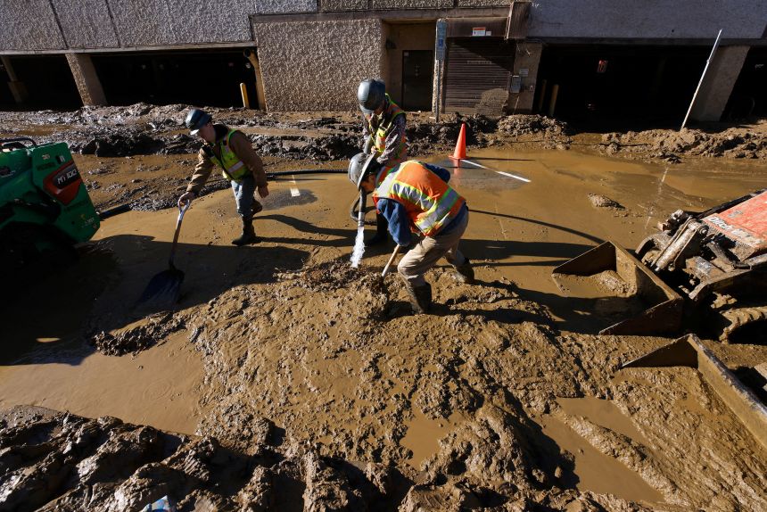 Workers work to clear mud from the streets of the Biltmore Village district two weeks after Hurricane Helene, in Asheville on October 11, 2024.