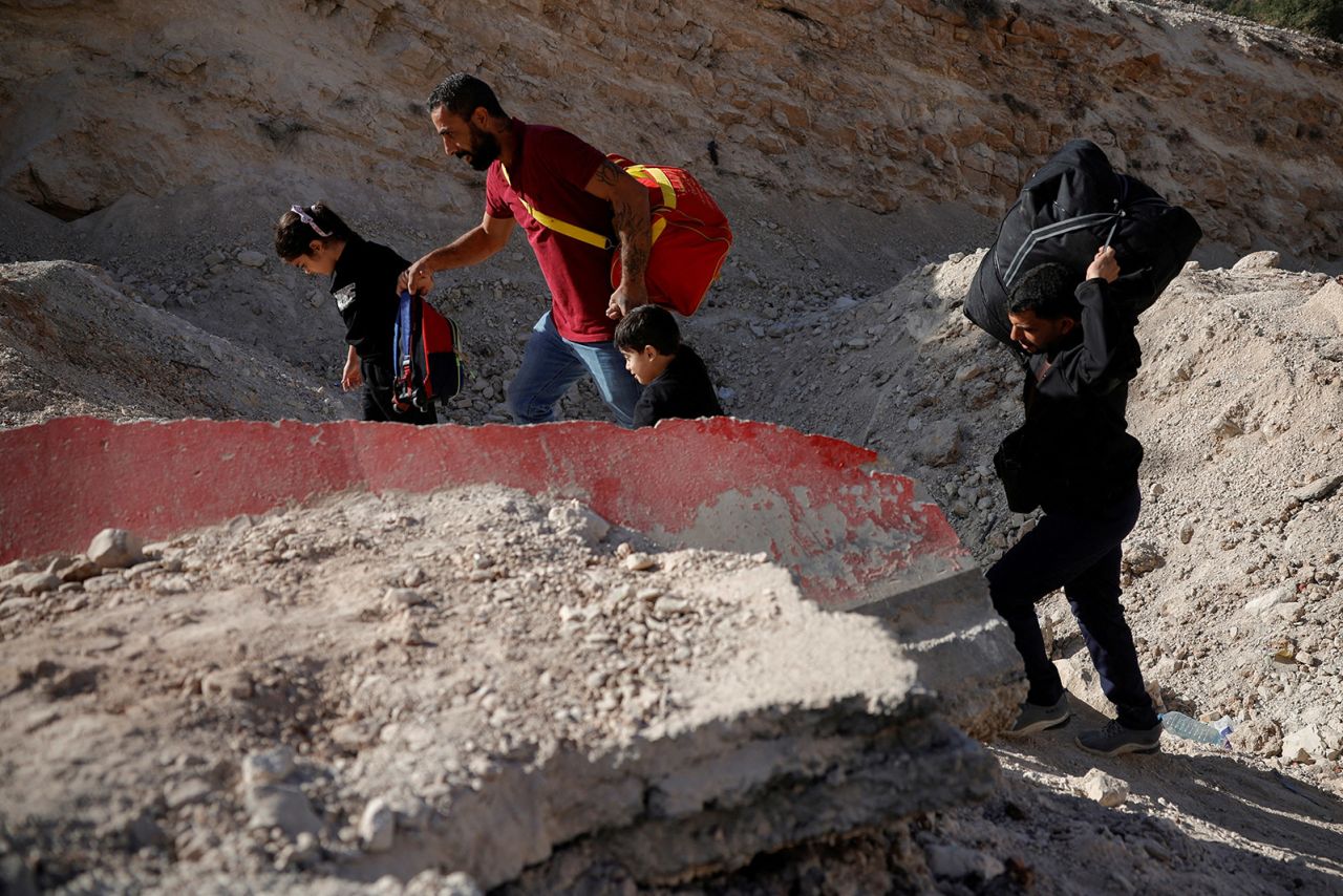 A man helps his children to walk through a crater while crossing from Lebanon into Syria, at the Maasna border crossing between Lebanon and Syria, October 14, 2024.