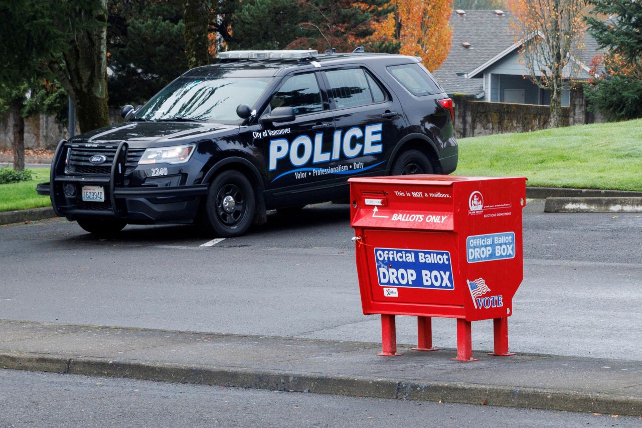 Officer Tyler Knott of the Vancouver Police Department surveils ballot boxes, where a freshly replaced ballot box stands in the Fisher's Landing Transit Center, in Vancouver, Washington, on October 29.