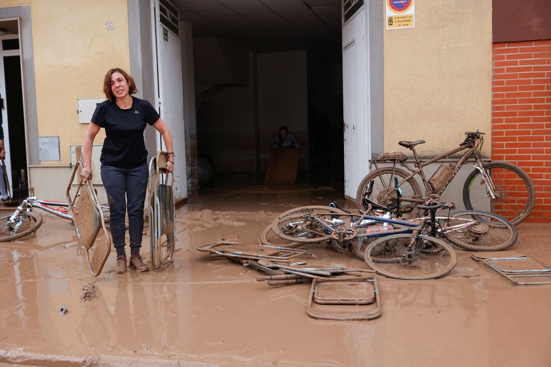 Een vrouw draagt ​​stoelen die onder de modder zitten nadat hevige regenval overstromingen veroorzaakte in La Alcudia, in de Spaanse regio Valencia.