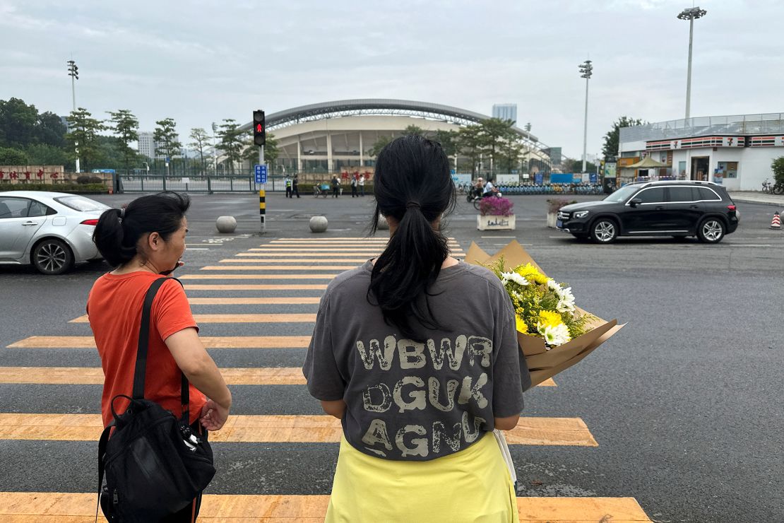 A woman carrying a floral tribute walks toward the sports center.