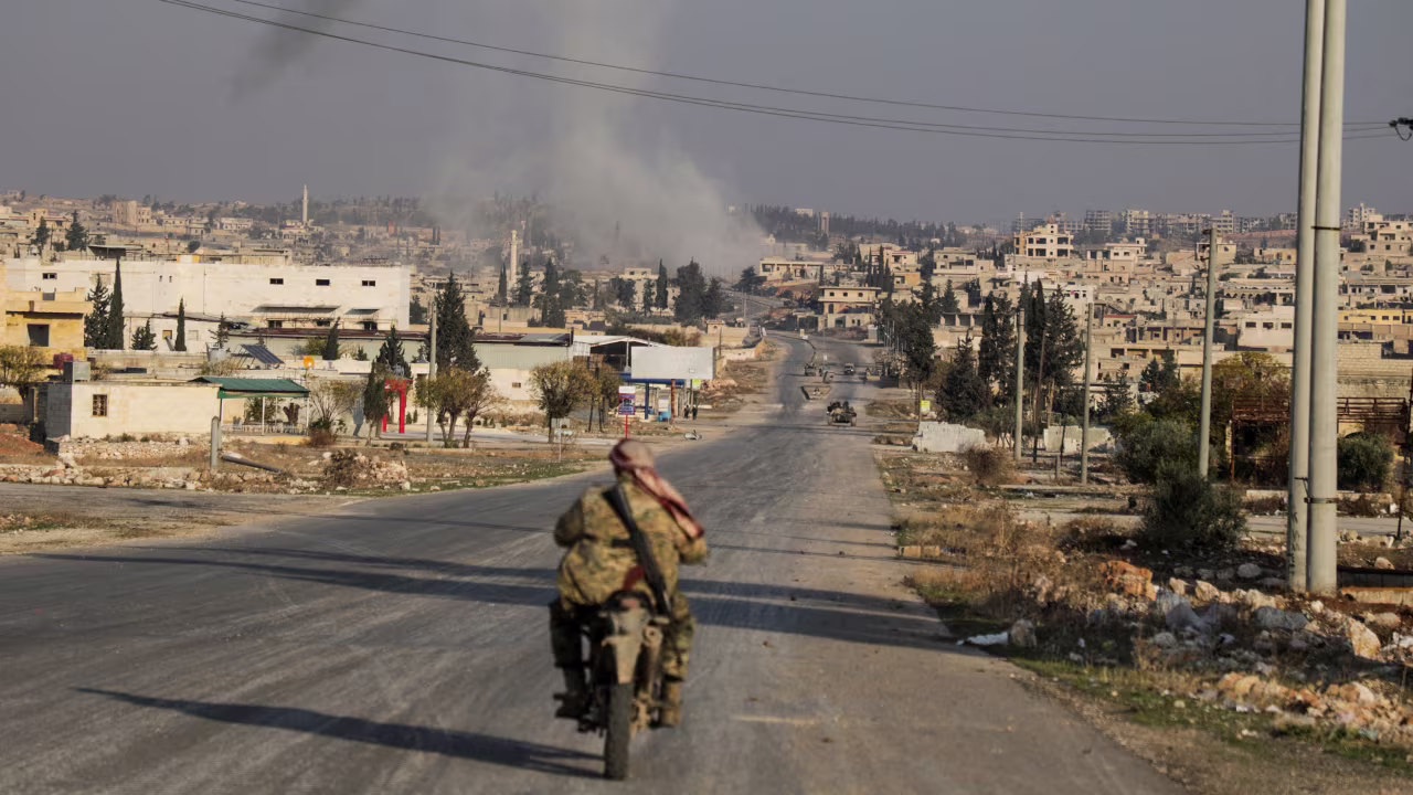 Smoke rises as a member of the rebels, led by the group Hayat Tahrir al-Sham, drives on a motorbike in al-Rashideen in Aleppo, Syria, on November 29.