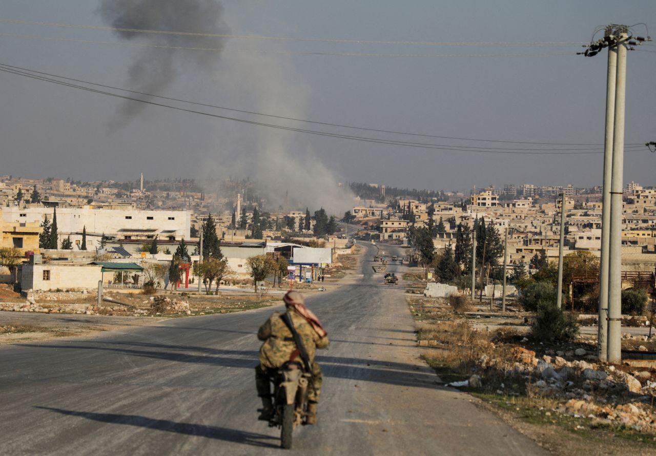 Smoke rises as a member of the rebels, led by the group Hayat Tahrir al-Sham, drives on a motorbike in al-Rashideen in Aleppo, Syria, on November 29.