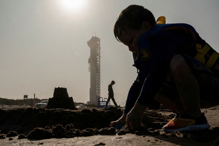 A boy builds a sandcastle on the beach as SpaceX's Starship sits on the launchpad ahead of the vehicle's third integrated test flight from the company's launchpad near Brownsville, Texas, on March 13, 2024.