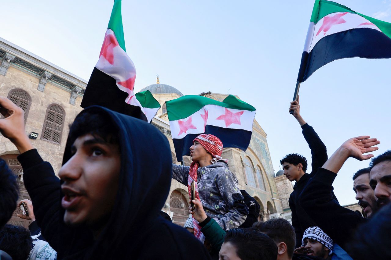 People wave the flag adopted by the new Syrian rulers on the first Friday after Syria's Bashar al-Assad was ousted, in the Damascus old city, on December 13.