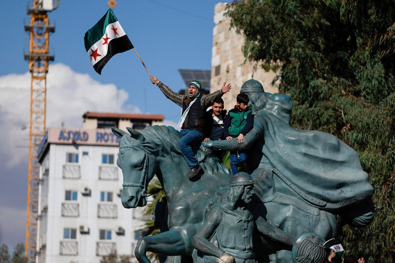 A man waves the new Syrian flag while on a statue of Saladin, the Arab leader who defeated the Crusade armies for the battle of Jerusalem, in Damascus, Syria, on December 13.