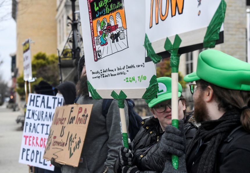 People carry placards and wear hats of the Nintendo character Luigi outside a court hearing involving Luigi Mangione.