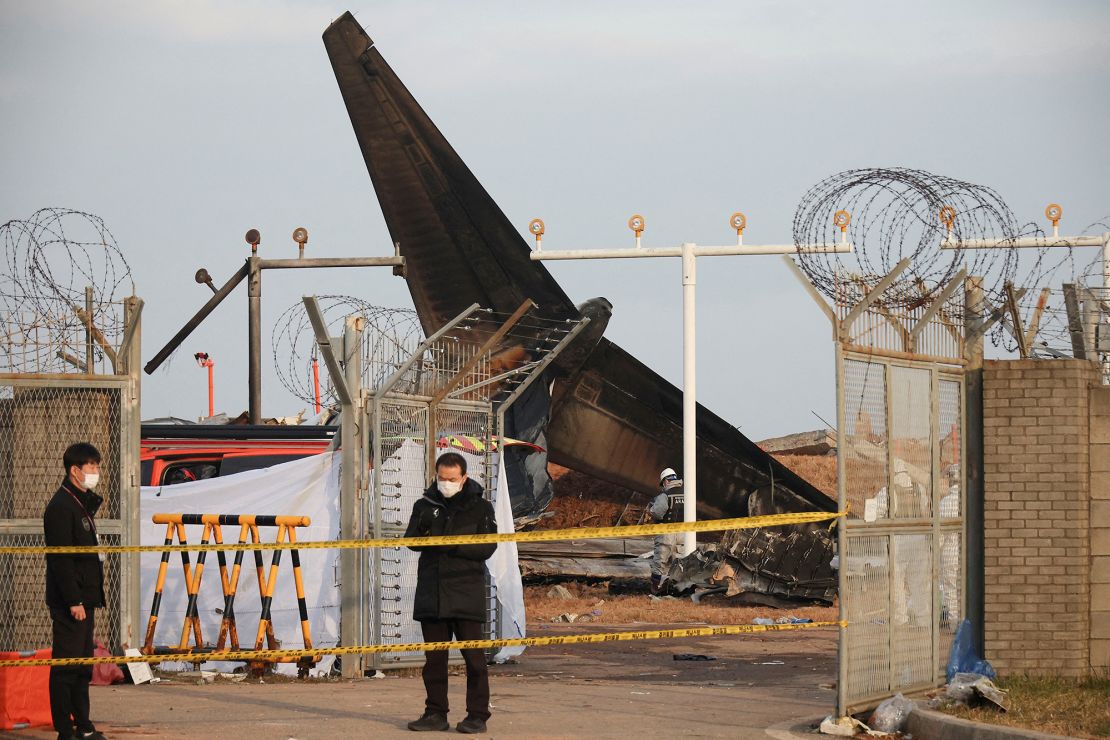 People stand at the site where an aircraft went off the runway and crashed at Muan International Airport, in Muan, South Korea, December 30, 2024.