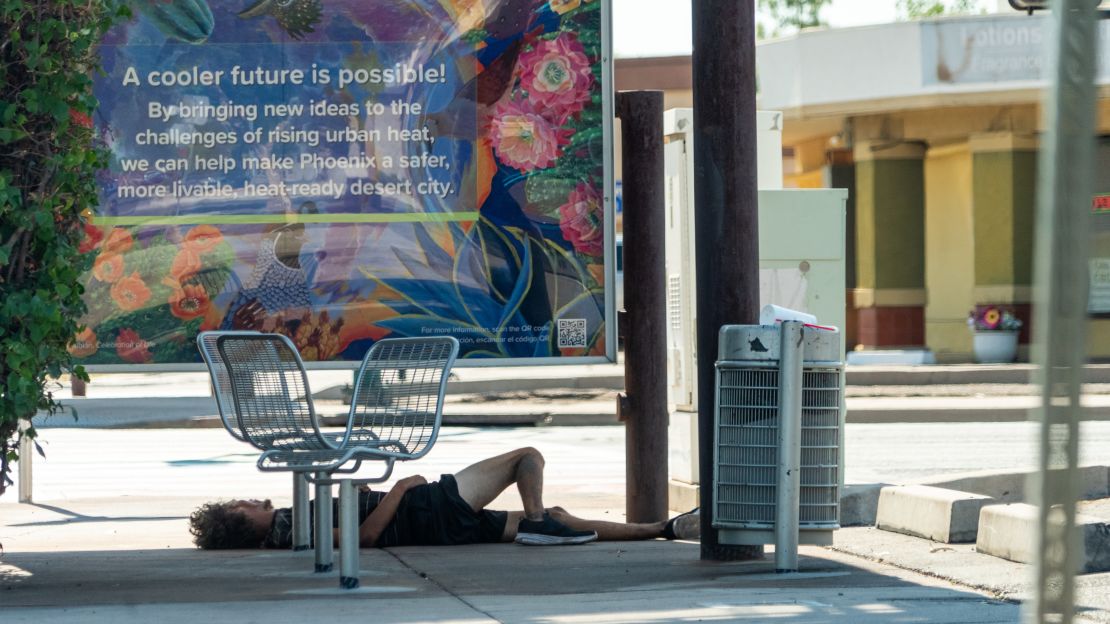 An unhoused man finds little respite from the heat in the shade of a bus stop in Phoenix.