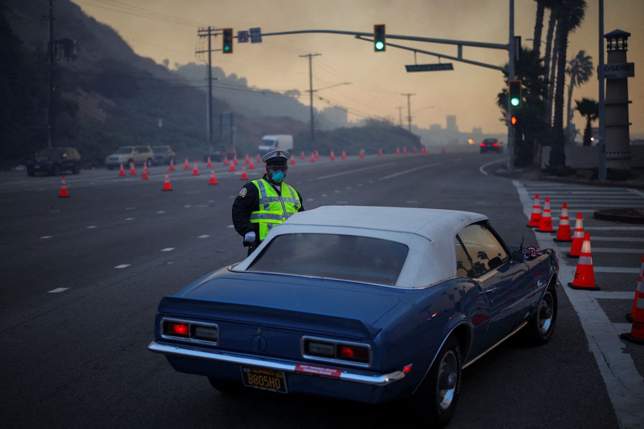 A police officer stands next to a vehicle Pacific Coast Highway as a wildfire burns in the Pacific Palisades neighborhood of west Los Angeles, California, on January 7.