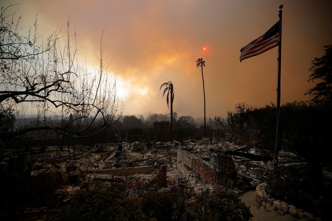 An American flag flies over the remains of destroyed homes as powerful winds fueling devastating wildfires in the Los Angeles area force people to evacuate, in the Pacific Palisades neighborhood of west Los Angeles.