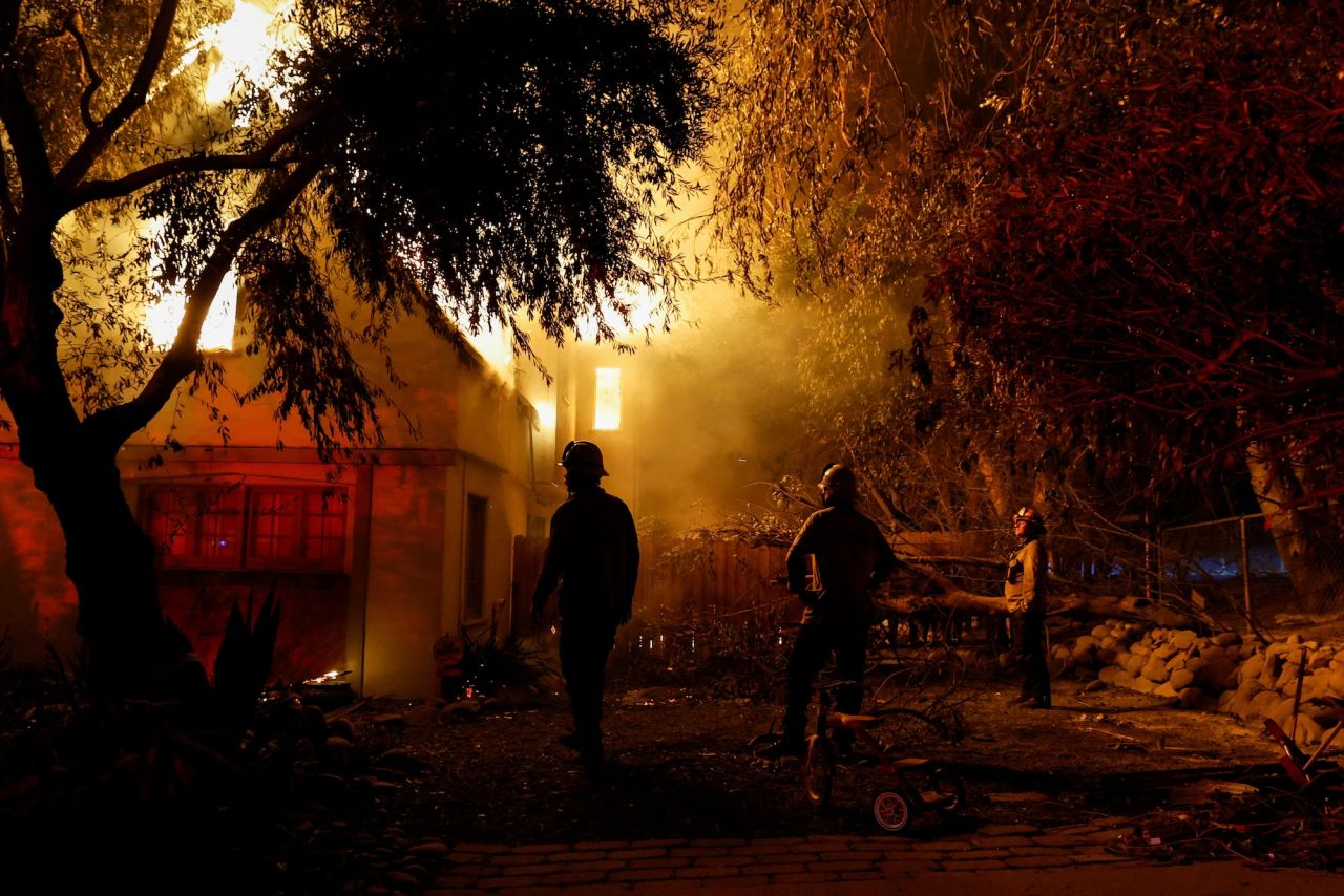 Firefighters stand near a burning house in Altadena on January 8.