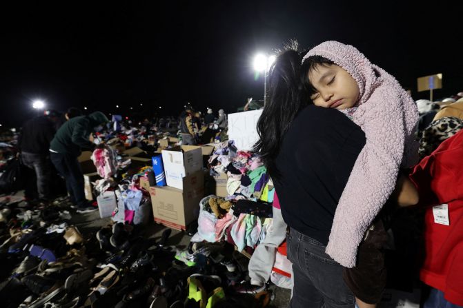 A girl sleeps on her mom's shoulder at a distribution center that was set up for people affected by the Eaton Fire.